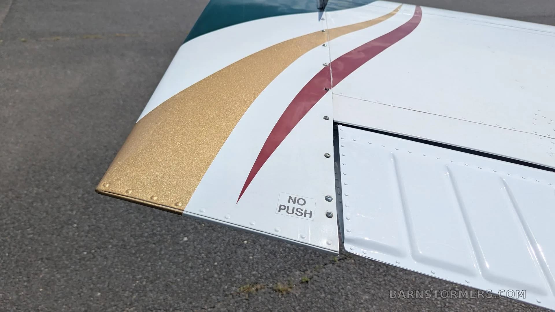 A close-up of the wingtip of the Beechcraft Bonanza, featuring gold and maroon stripes and a "NO PUSH" label.