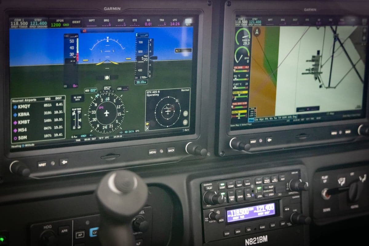 A close-up of the aircraft's cockpit showing two Garmin G1000 NXi displays with flight information and navigation data.
