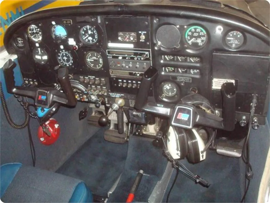The instrument panel and controls of a small aircraft cockpit, with blue seats visible.
