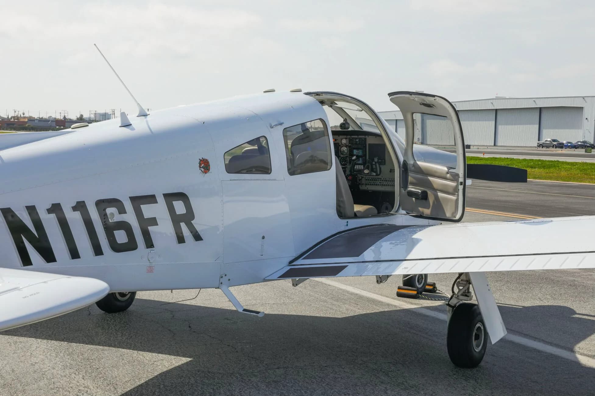 A close-up side view of the white Piper PA-28-181 Archer III aircraft with its door open, showing the cockpit.