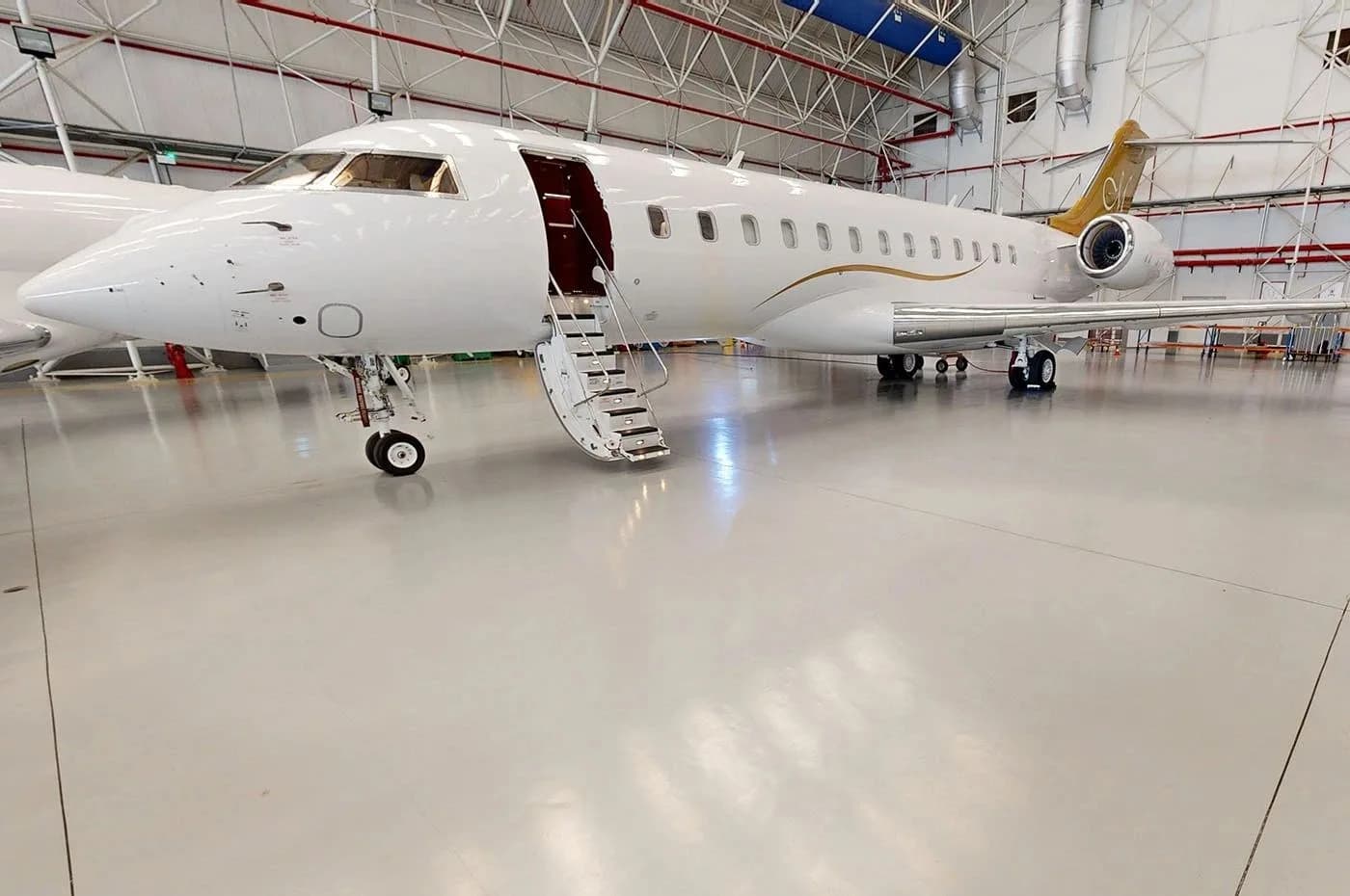 A white business jet with gold accents on the tail and fuselage, parked in a hangar with its main door open and stairs extended.