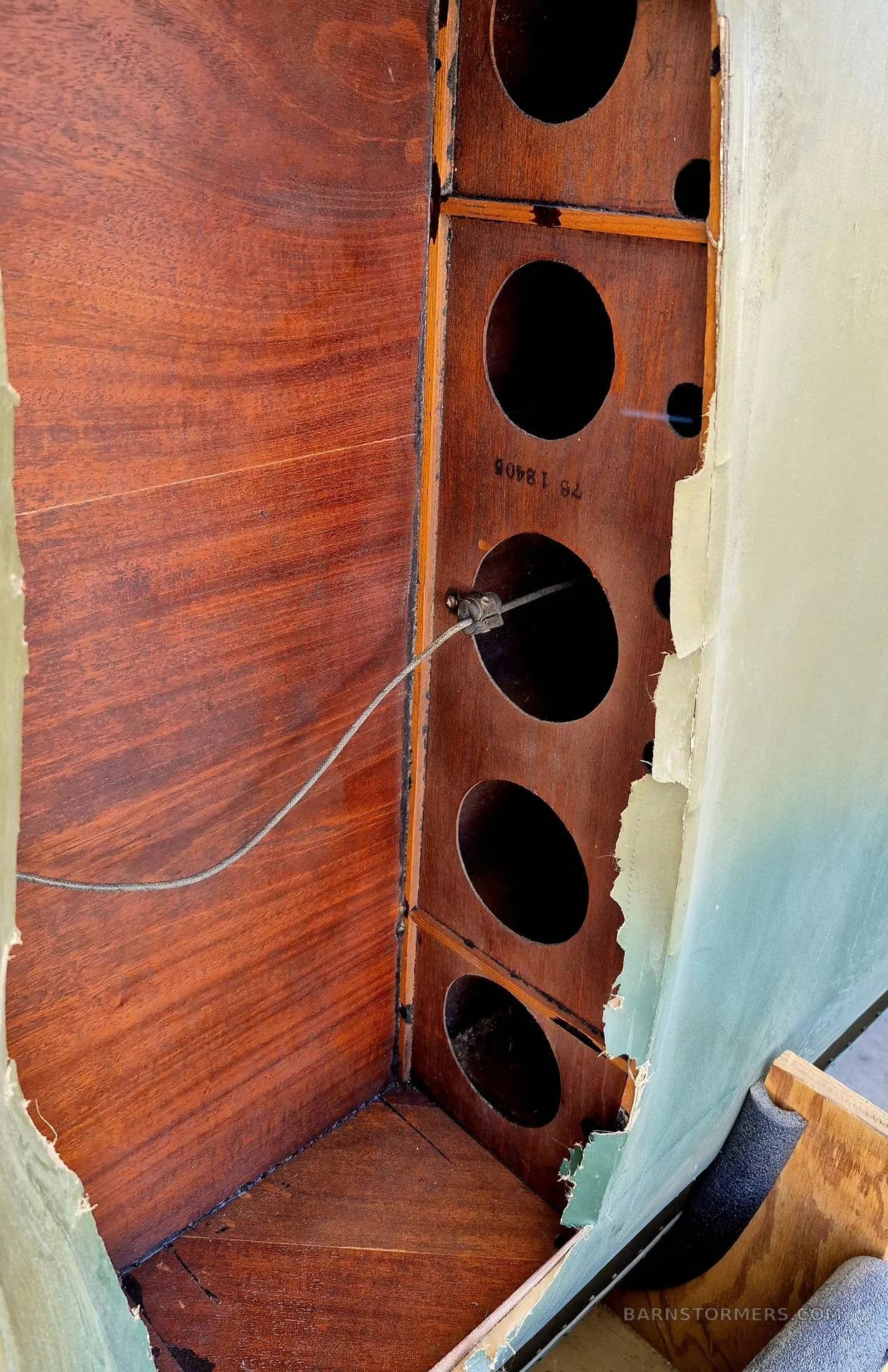A close-up view of internal aircraft structure, showing wooden ribs with circular cutouts and a control cable.