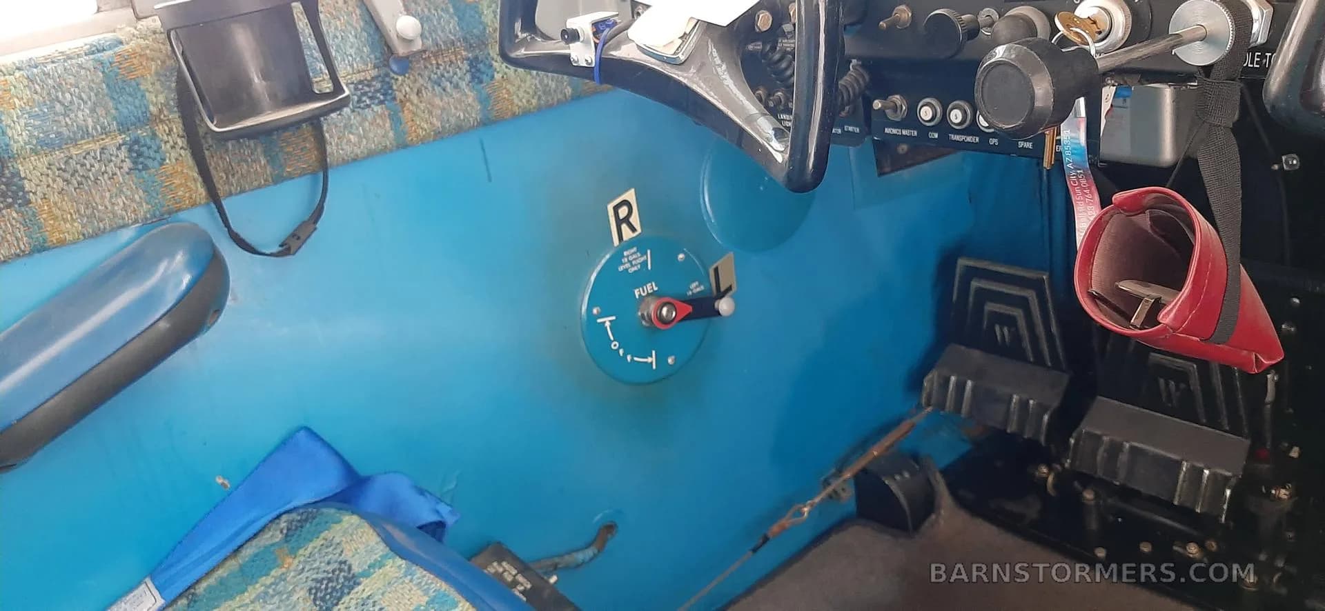 The interior of an aircraft cabin, showing blue flooring, rudder pedals, and a fuel selector switch.