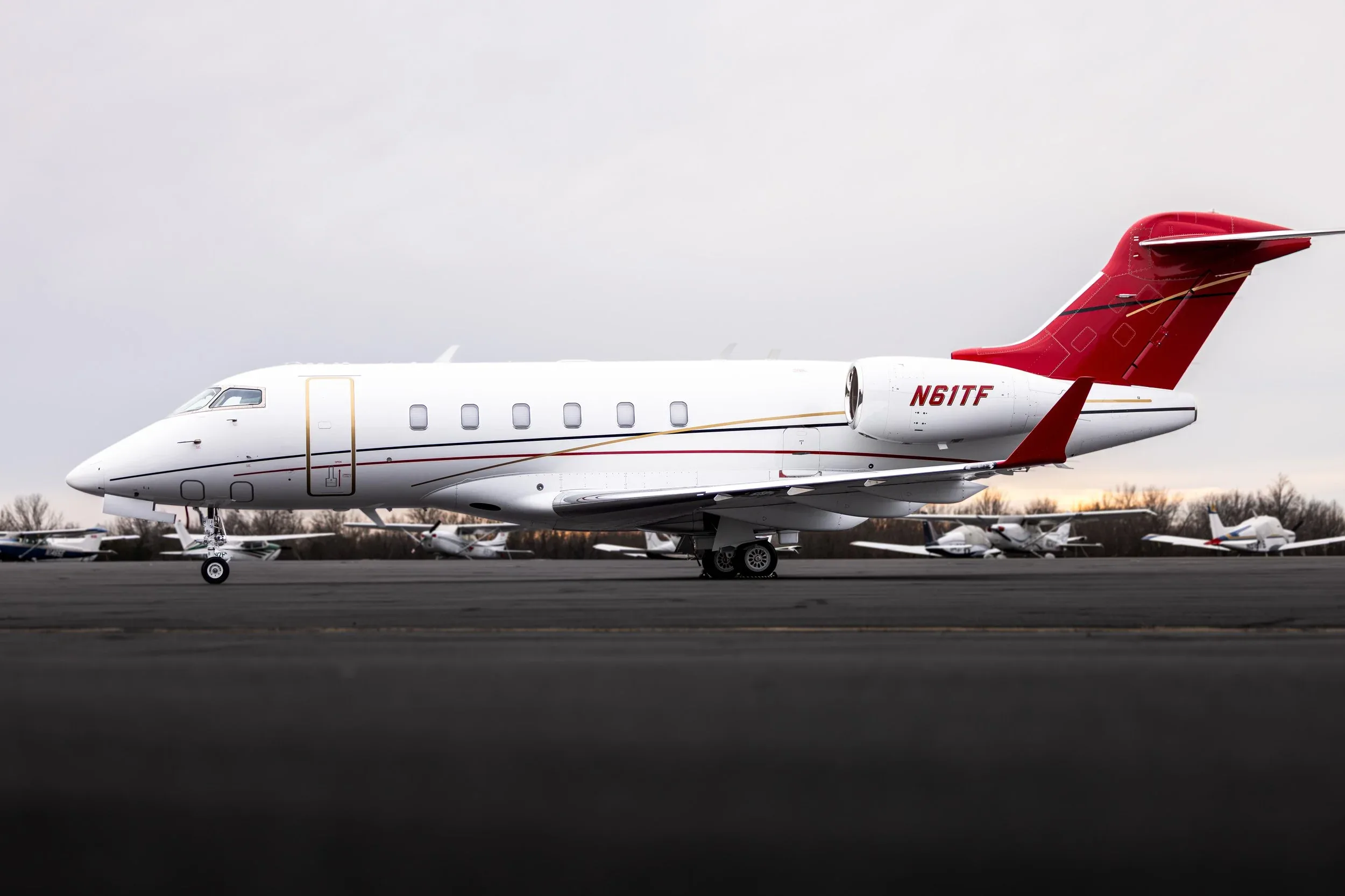 Side view of a white and red Bombardier Challenger 300 aircraft with registration N61TF on the tarmac.