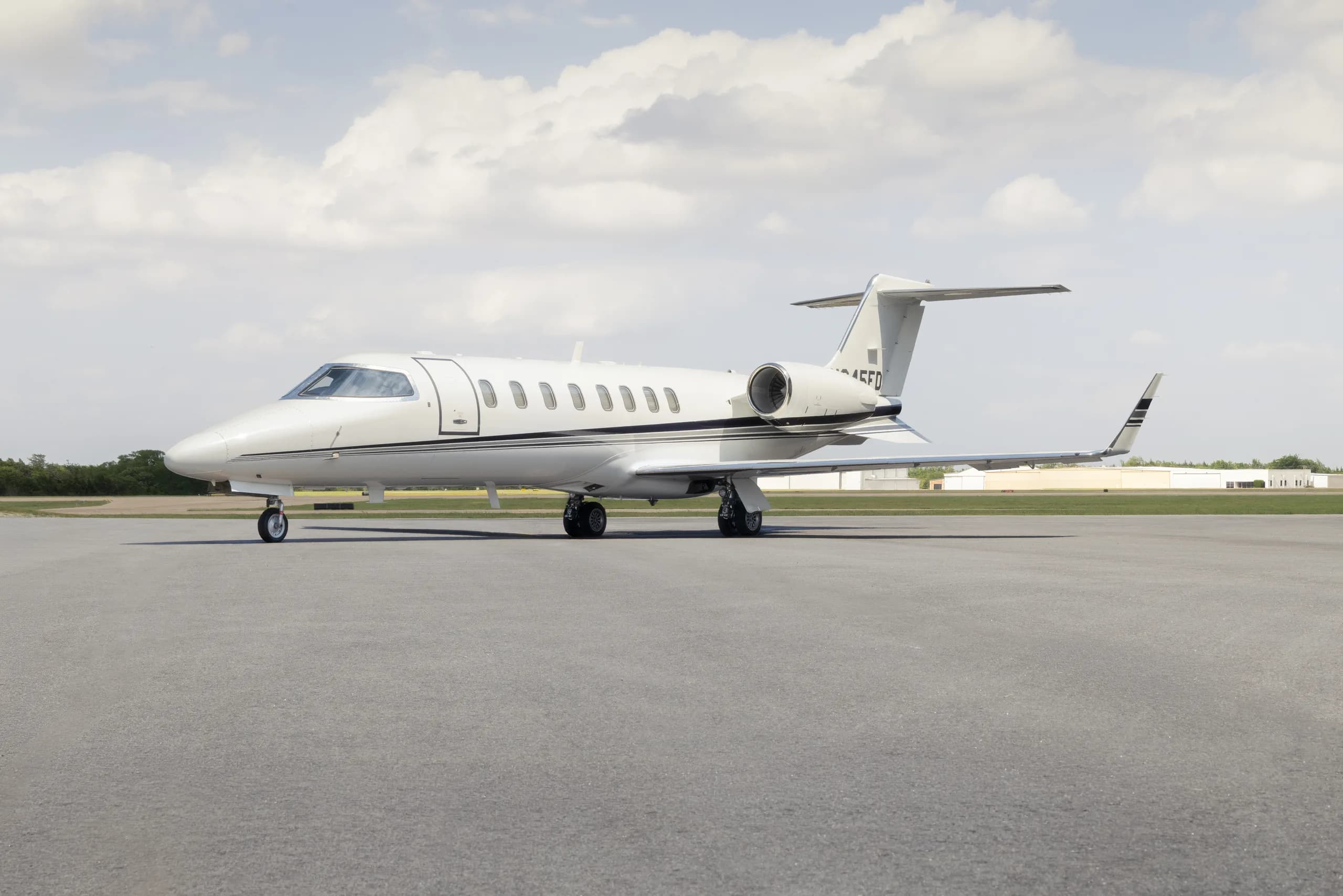 A white Learjet 60 with black stripes on the tail and engines, registered N645FD, parked on an asphalt runway under a partly cloudy sky.