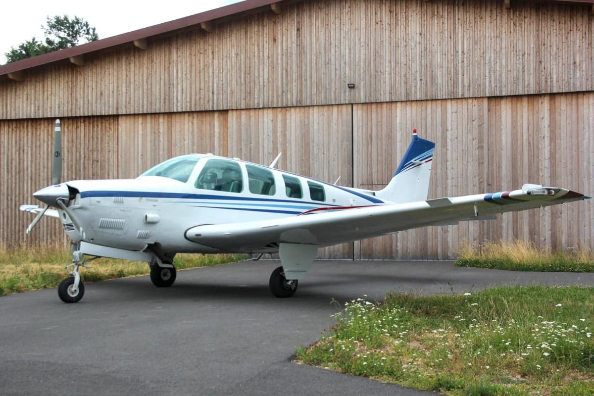 Side view of N225CR Beechcraft Bonanza parked in front of a hangar.
