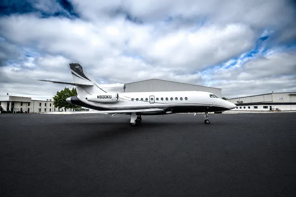 A Dassault Falcon 900EX business jet, registration N900KU, parked on a tarmac with airport buildings in the background.
