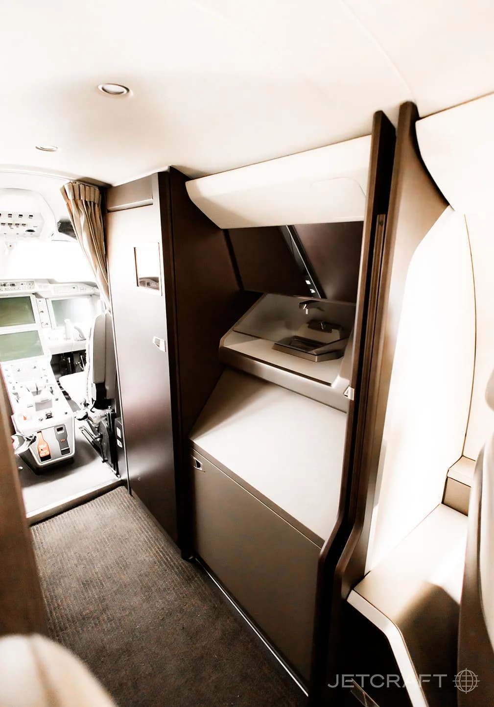 A view of the aircraft's galley or storage area, with shelves and cabinetry, located near the cockpit entrance.