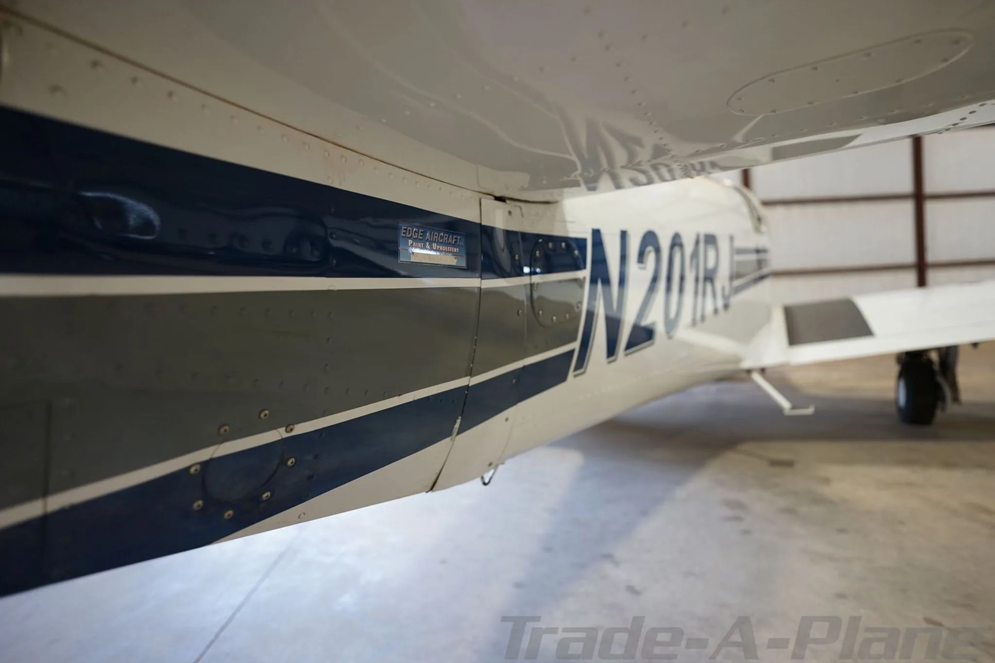 A close-up view of the white fuselage of aircraft N201RJ, showing blue and grey stripes and rivets.