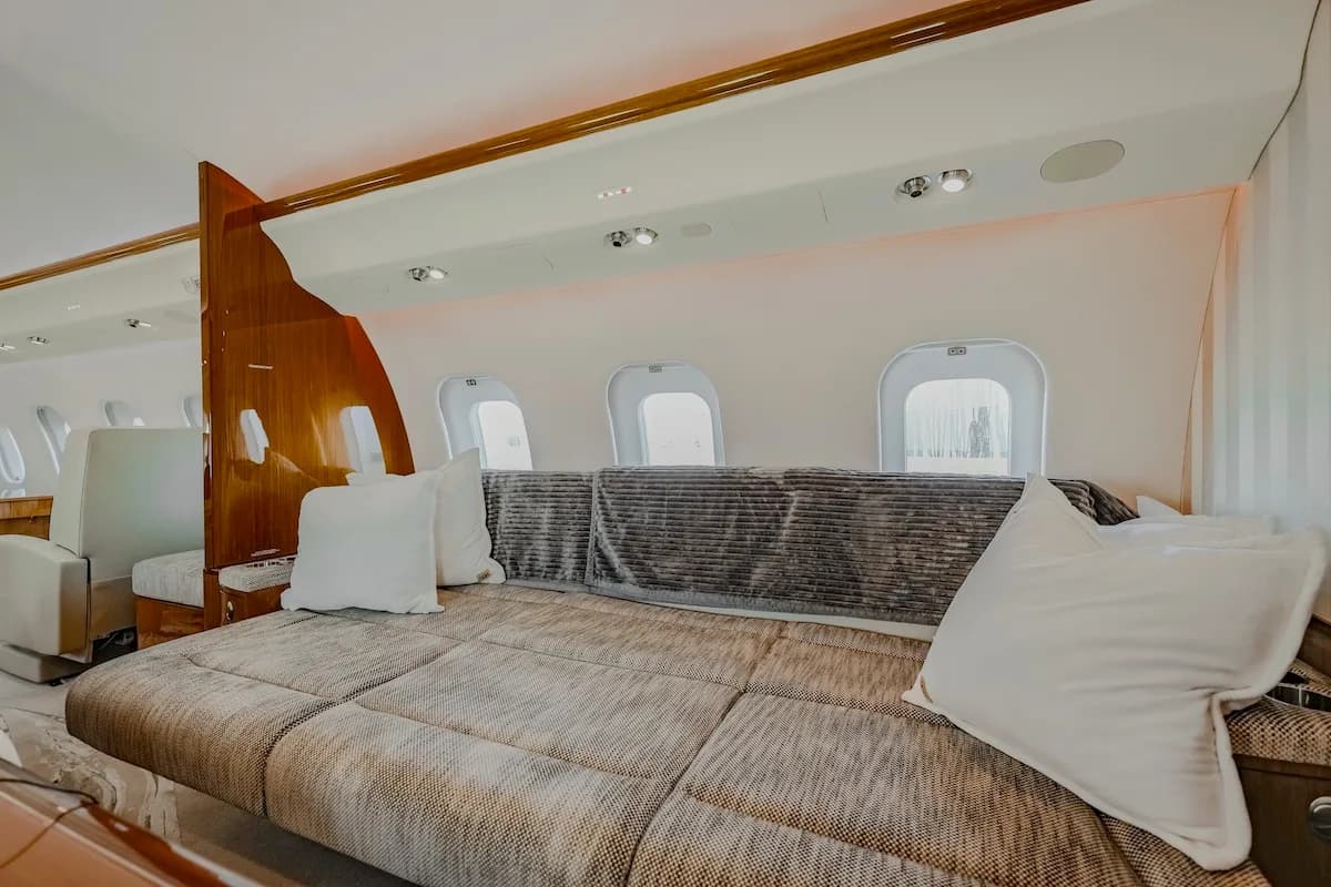 A comfortable aircraft cabin interior featuring a large, upholstered sofa with pillows next to windows.