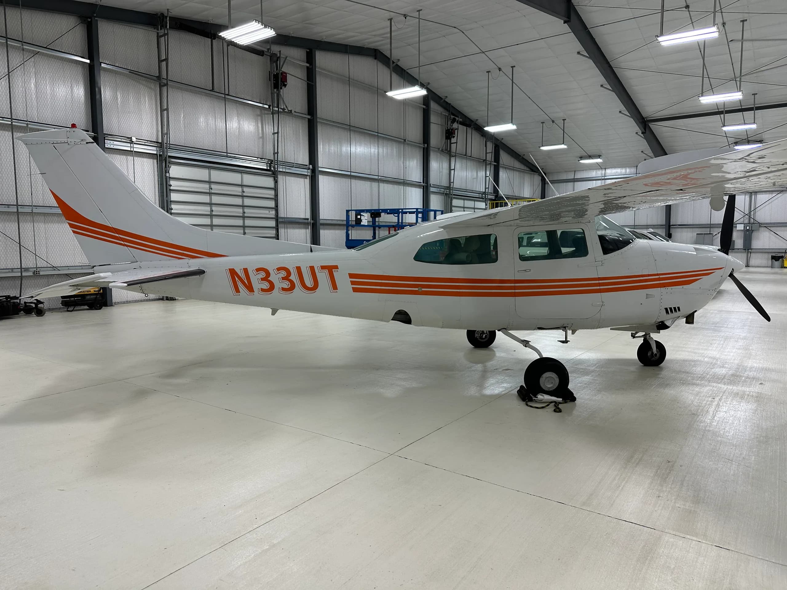 A Cessna 206 Stationair aircraft with orange stripes parked in a hangar.