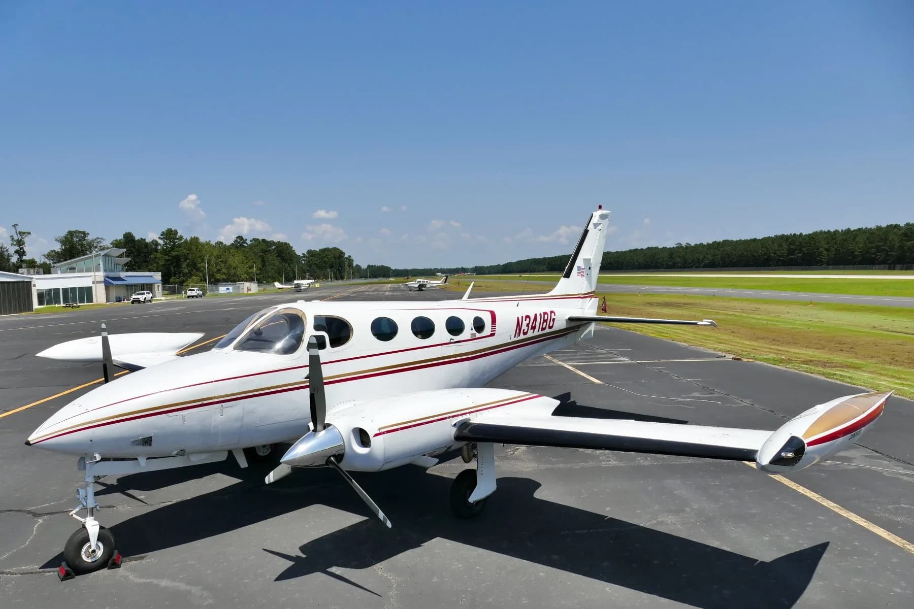 Front three-quarter view of a white twin-engine propeller aircraft N341BG on an airfield with a runway in the background.