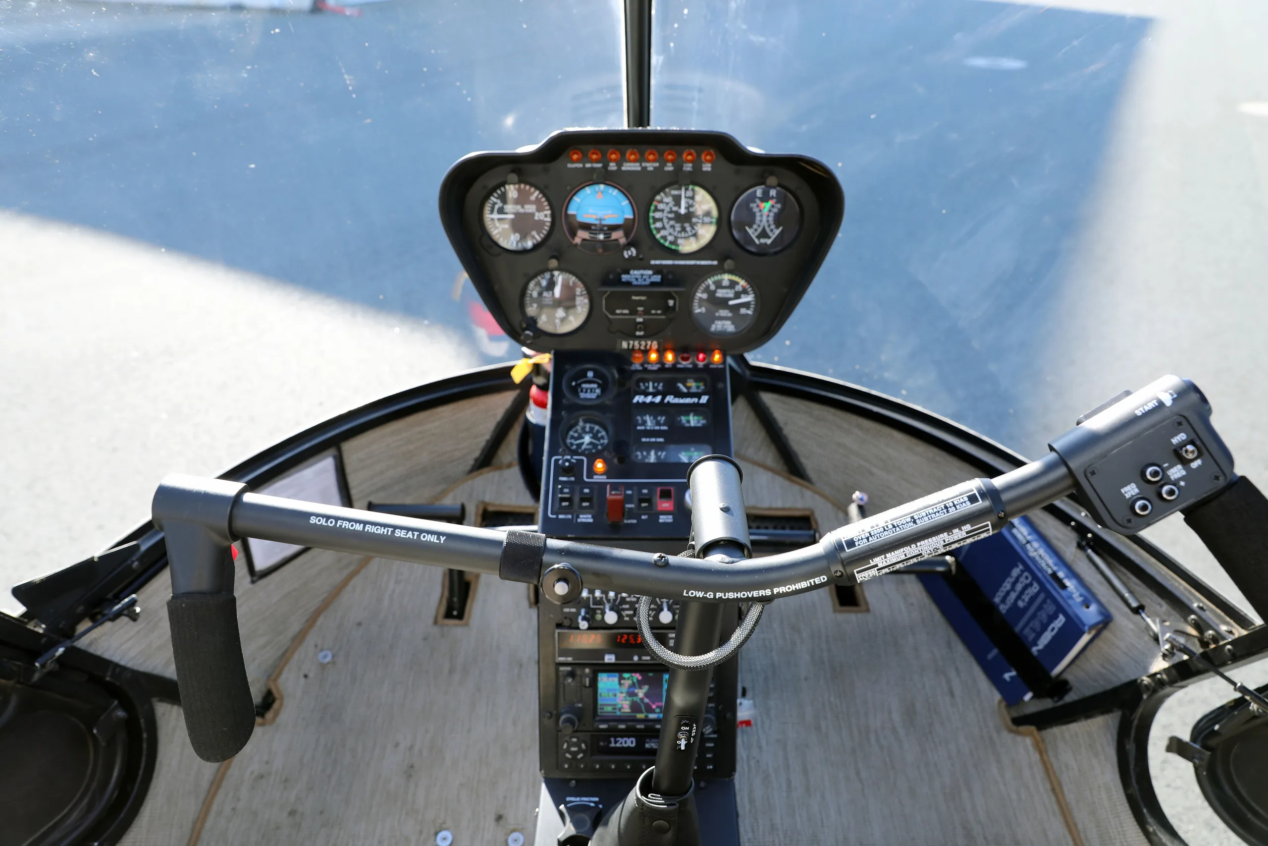 Overhead view of the Robinson R44 Raven II helicopter cockpit, showing the instrument panel and cyclic control.
