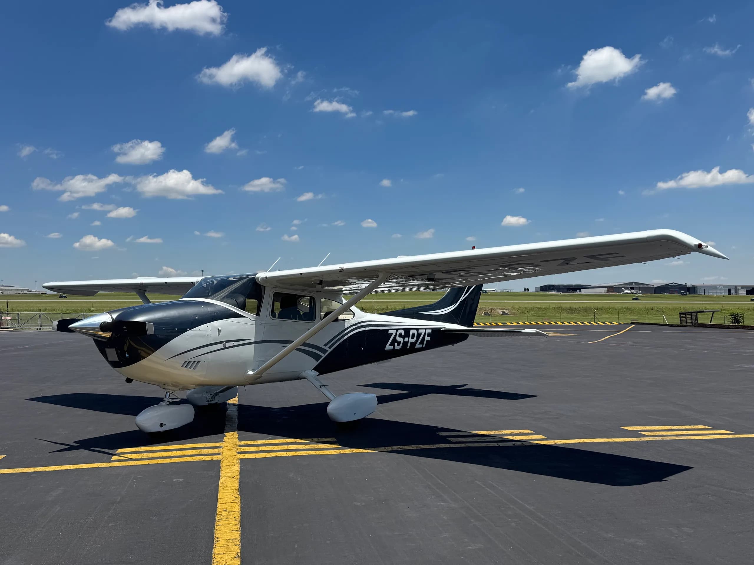 A white and black Cessna high-wing aircraft parked on the tarmac under a blue sky.