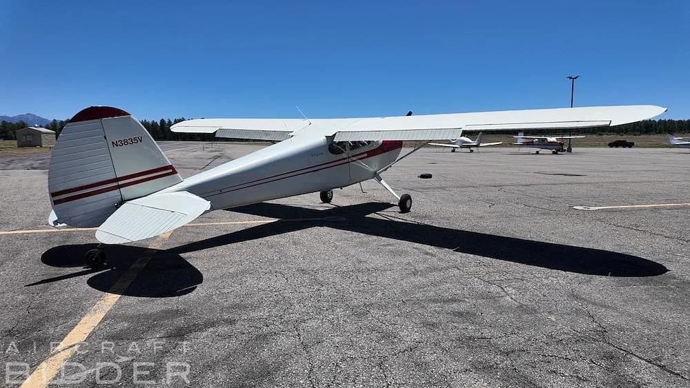 A rear view of a white 1950 Cessna 170A aircraft (N3835V) with red stripes, parked on an airfield.