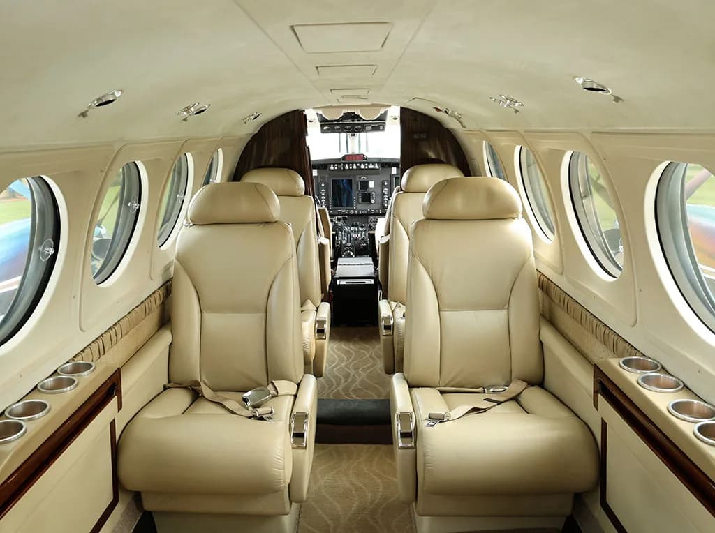 The interior cabin of a private jet with beige leather seats and a view into the cockpit.