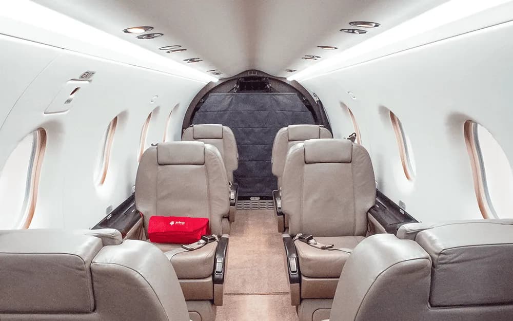 The interior cabin of a private aircraft with beige leather seats and a red bag on one of the seats, looking towards the rear.