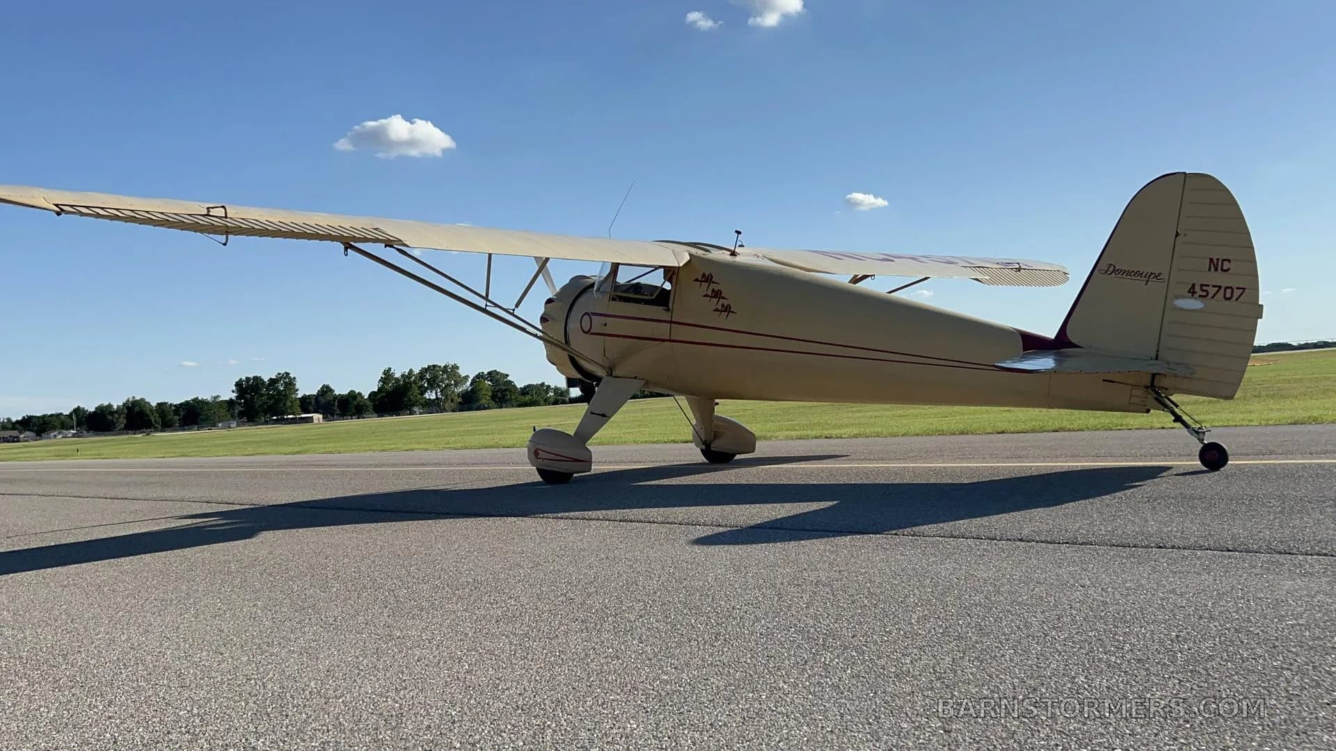 A cream-colored vintage aircraft with red pinstripes and registration NC45707 on the tail, parked on an asphalt runway.