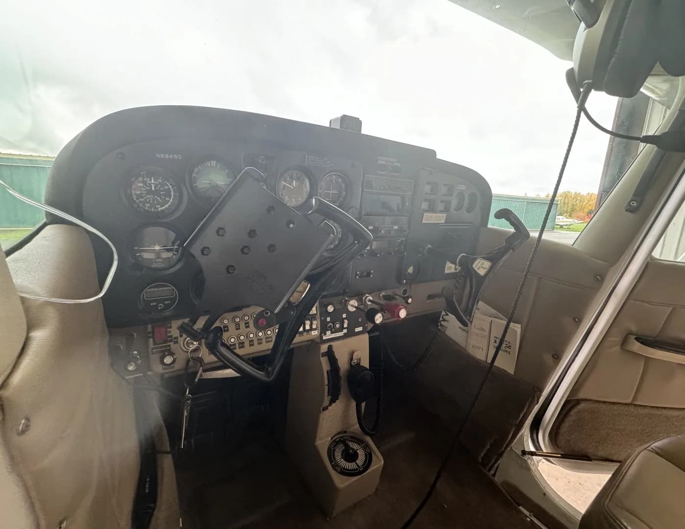 The cockpit of a light aircraft features a dark instrument panel with various gauges and controls, and a yoke with a tablet mount.