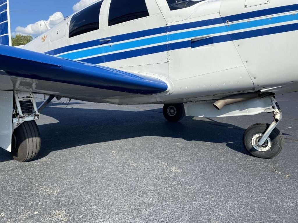 Close-up of the landing gear and underside of the wing of the Mooney M20C aircraft.