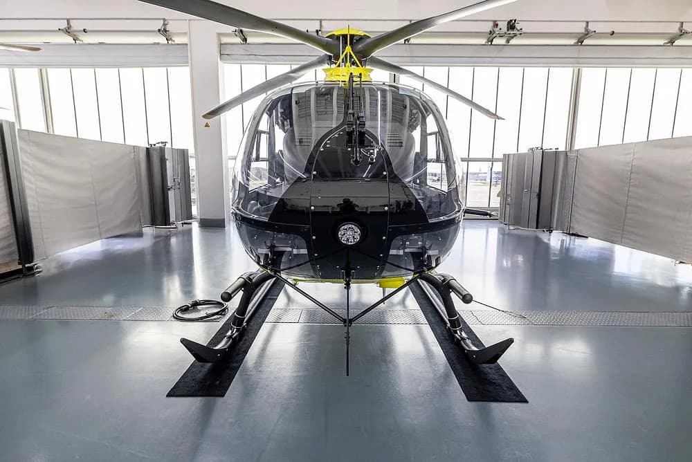A bright yellow Airbus H135 helicopter is viewed head-on inside a hangar, showing its large front windshield.