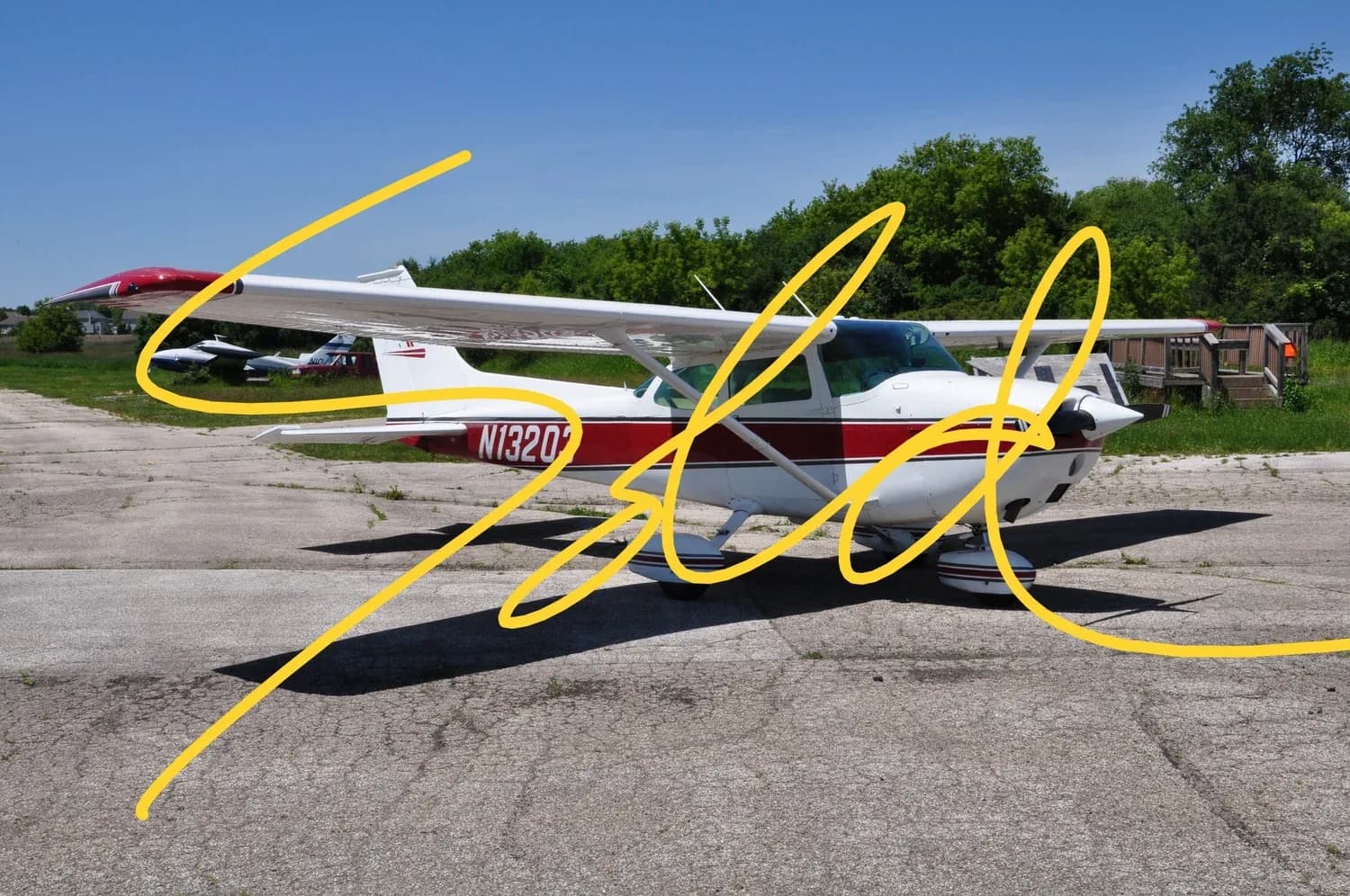 A white and red Cessna 172 aircraft (N13203) parked on an asphalt ramp under a clear blue sky.