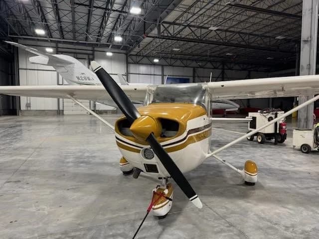 A front view of the white and gold Cessna aircraft, N64479, with its propeller, parked in a hangar.