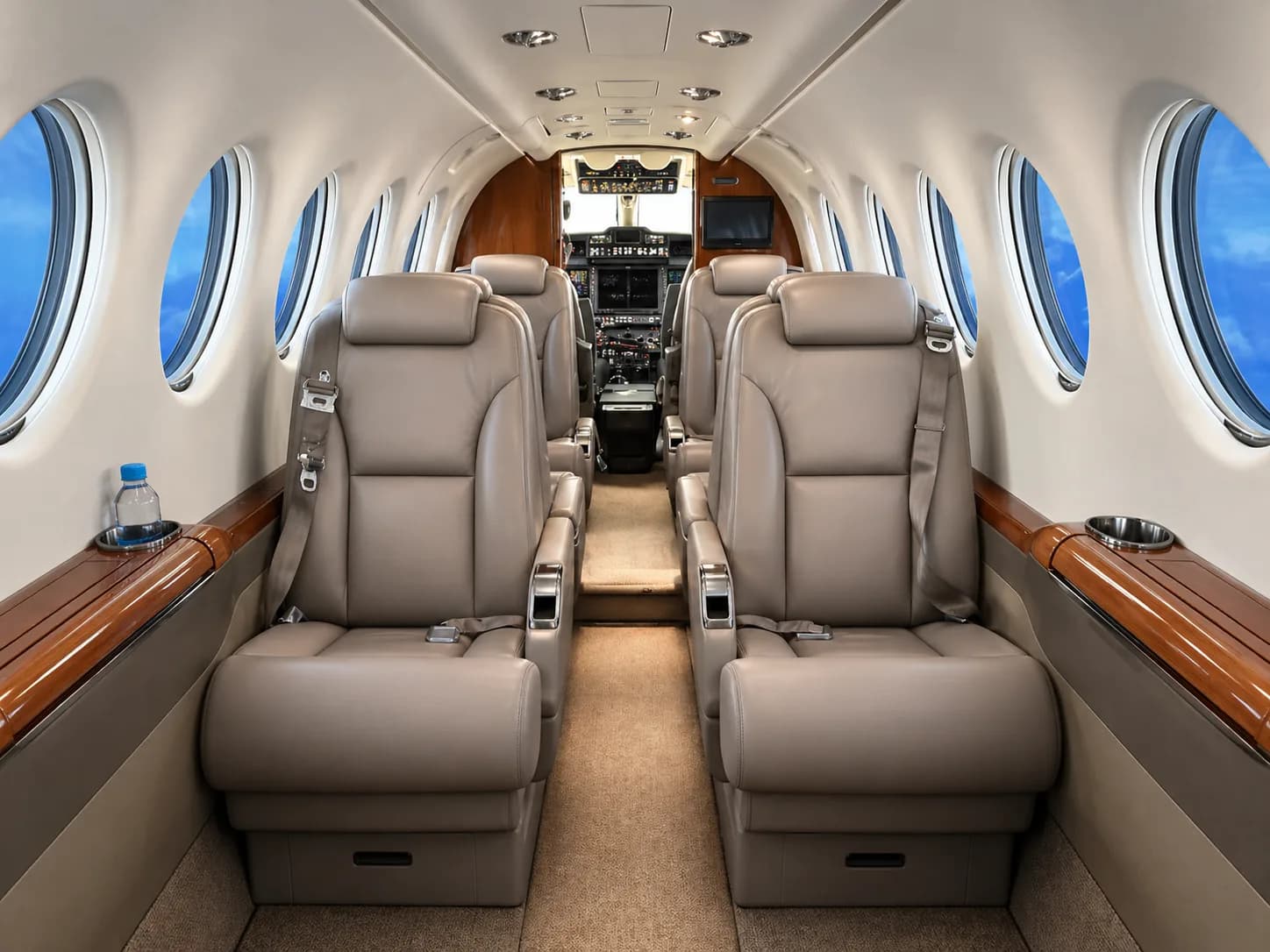 The luxurious interior cabin of a private aircraft with tan leather seats and large windows showing a blue sky.