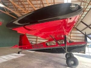 A red and black Cubcrafters aircraft with tail number N380K is parked inside a hangar.