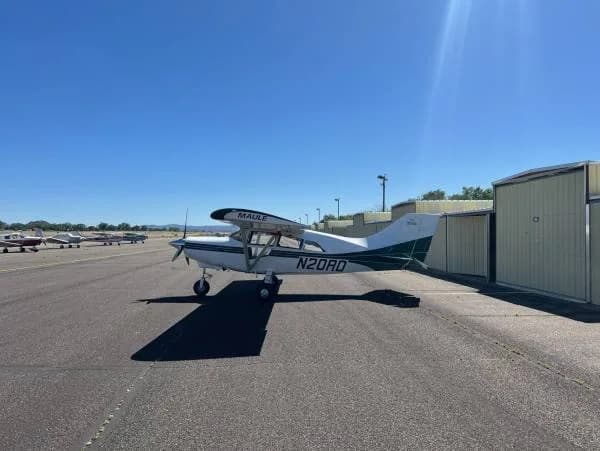 A white and green Maule aircraft, registration N20RD, parked on a tarmac with other aircraft in the distance.