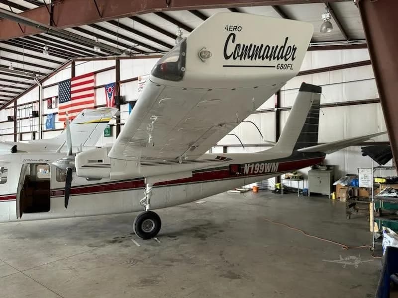 A rear-side view of a white and red Aero Commander 680FL twin-engine aircraft, registration N199WM, parked in a hangar.