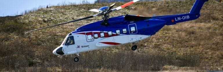 A blue and white Bristow helicopter is in flight over a field.