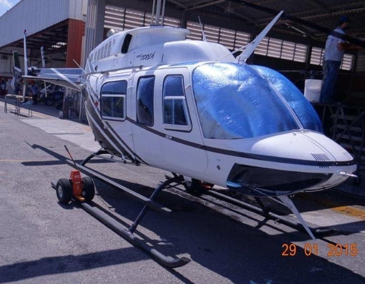 A white and black Bell 206L helicopter with blue sunshades on the windshield, parked in a hangar.