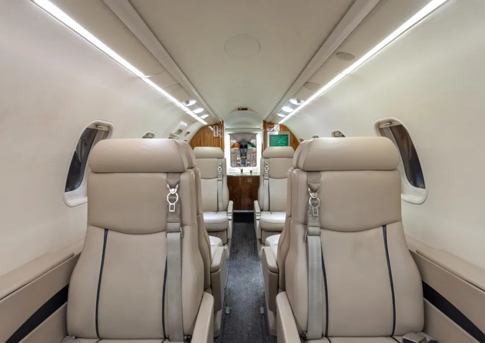 A view down the aisle of a business jet cabin, showing rows of beige leather seats.