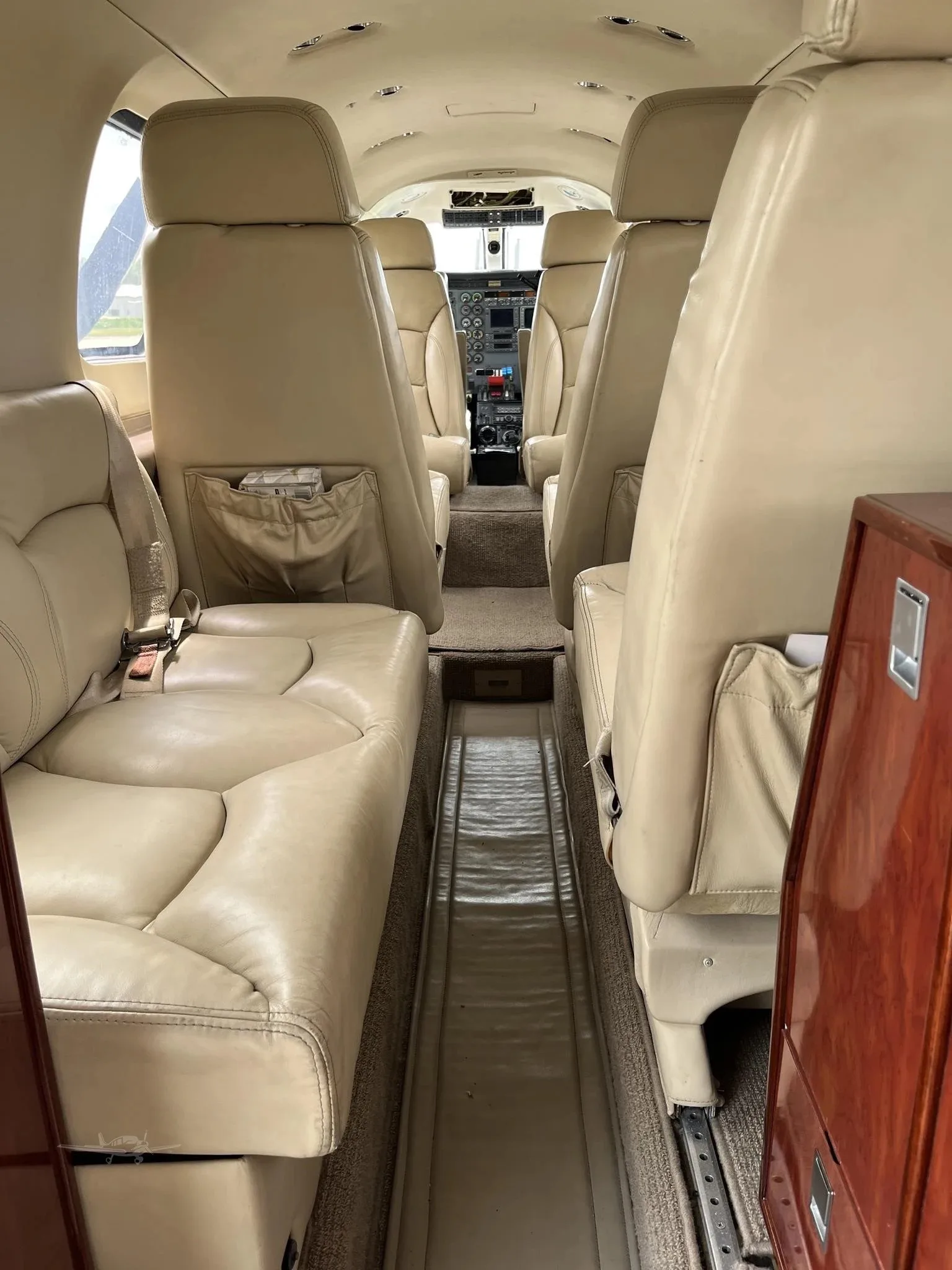 Interior view of the aircraft cabin, showing rows of beige leather seats leading towards the cockpit.