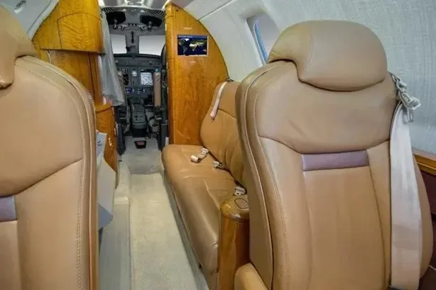 View from the aircraft cabin looking towards the cockpit, featuring tan leather seats and wood paneling.