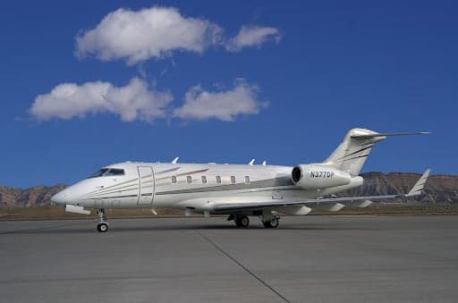 A Challenger 300 aircraft on the tarmac with mountains in the background.