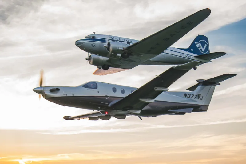 A Pilatus PC-12 and a Douglas DC-3 fly in formation at sunset.