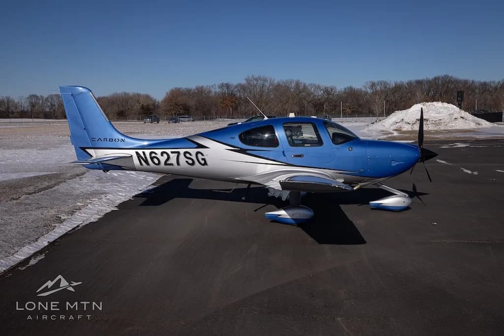 A side view of the blue and silver Cirrus SR22 aircraft (N627SG) on a snowy tarmac.