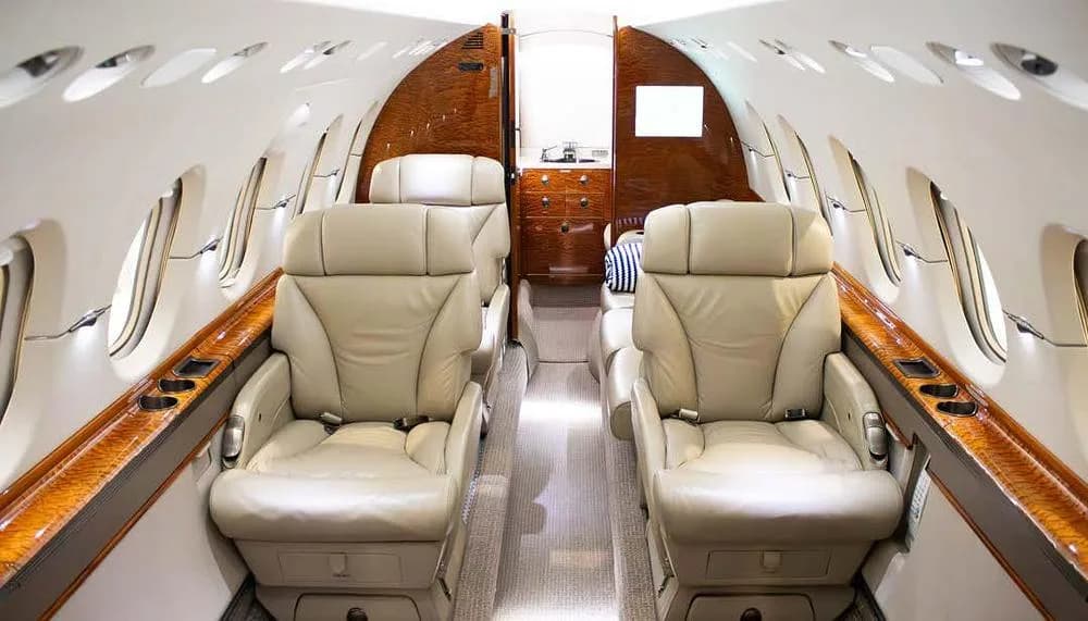 The luxurious interior cabin of a private jet with light beige leather seats and polished wood accents.