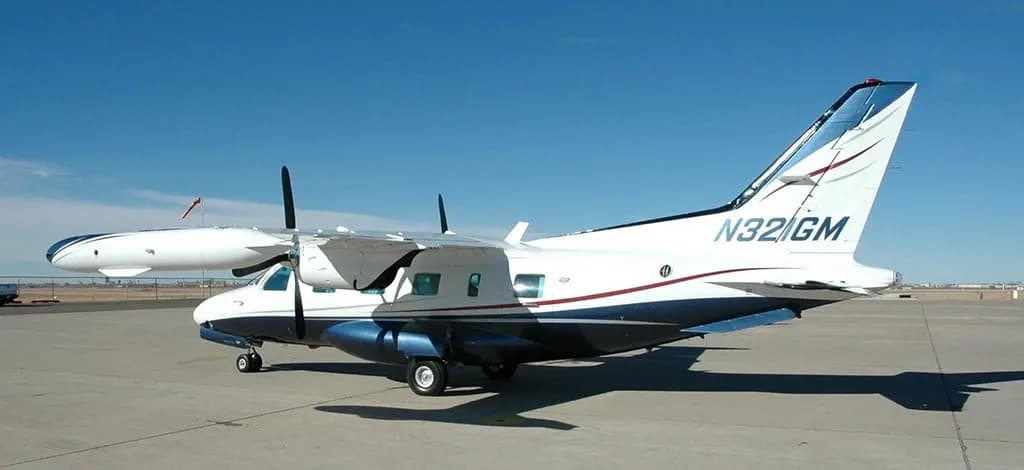 A three-quarter rear view of a white and blue twin-engine turboprop aircraft, registration N321GM, parked on an airfield.