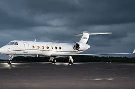 A white private jet parked on a wet runway under a cloudy sky.