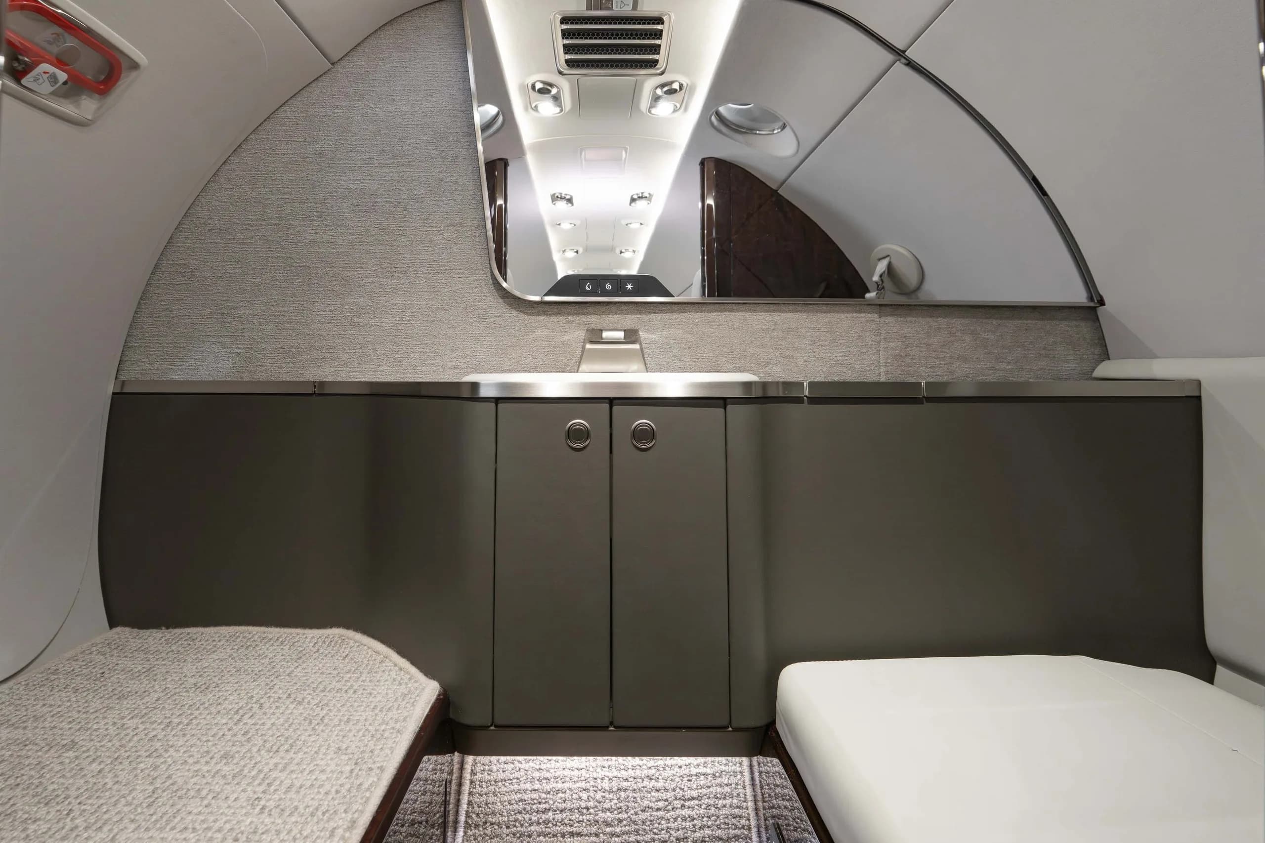 The lavatory or galley area of the business jet, featuring a counter, cabinets, and a mirror reflecting the cabin.