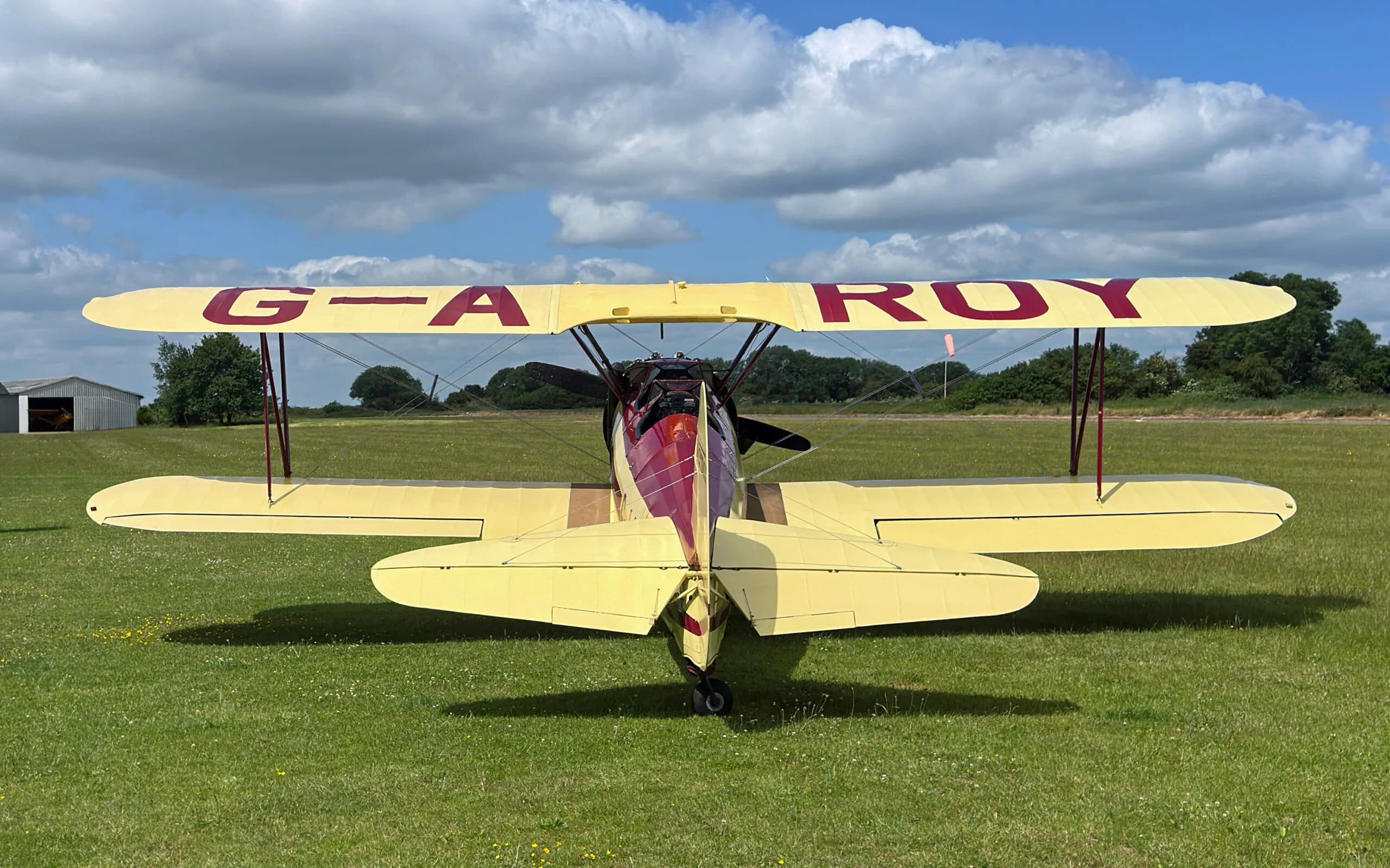 A rear view of the yellow and red Stearman biplane, G-AROY, showing its biplane wings and tail.