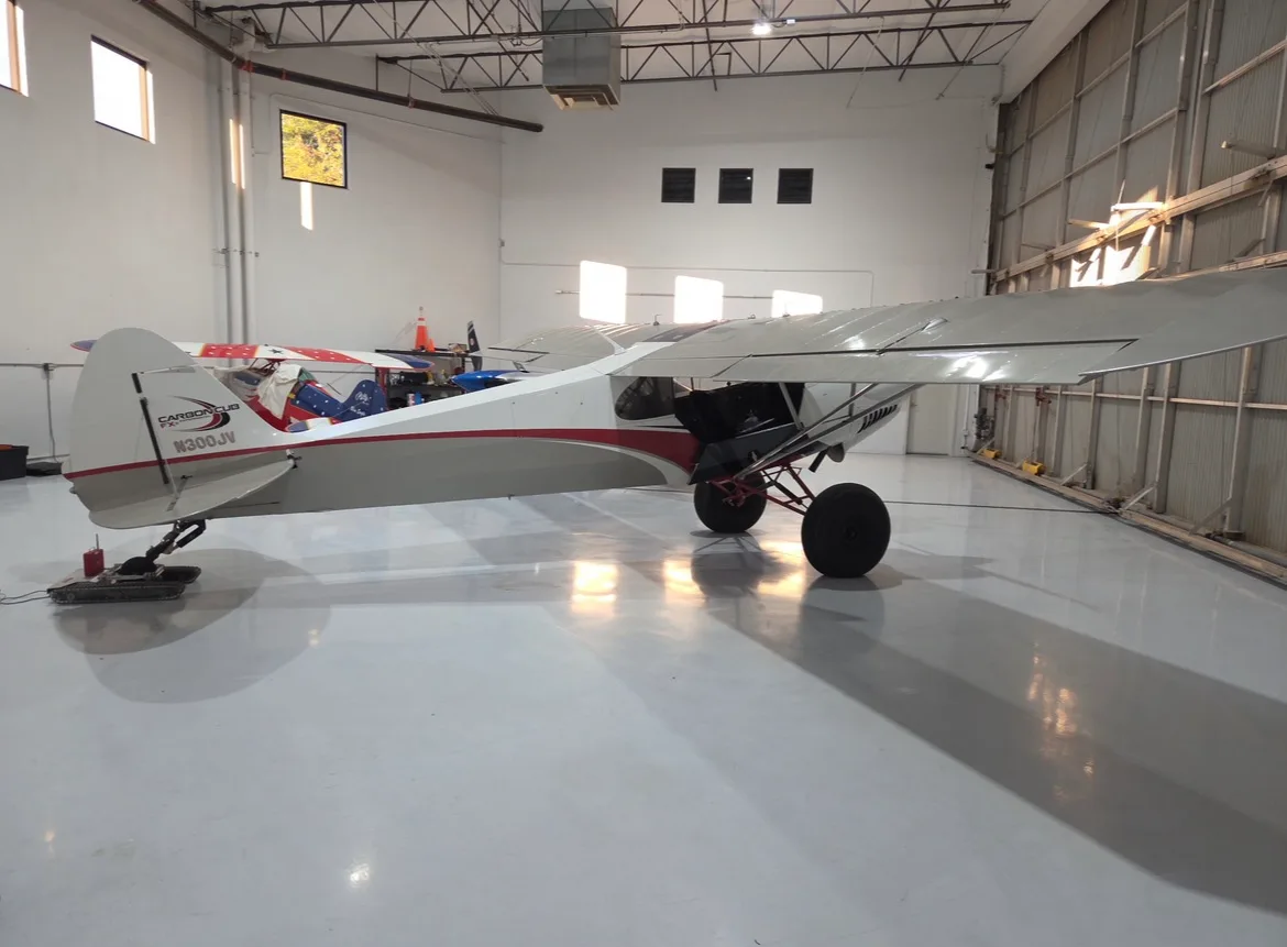 A Carbon Cub FX3 in a hangar, showing the tail and side.