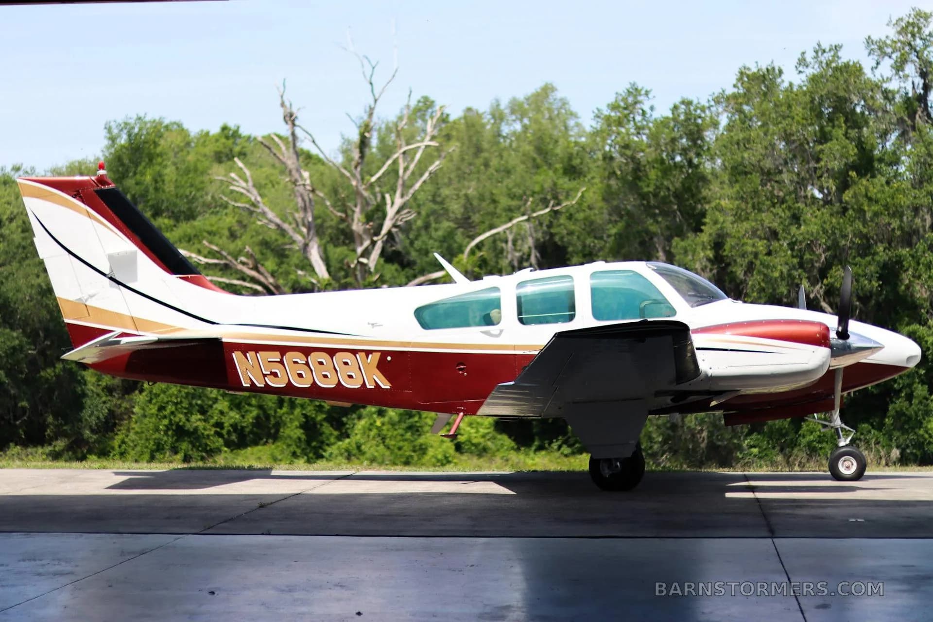 A side view of a white and maroon twin-engine propeller aircraft with registration N5688K, parked on a tarmac.