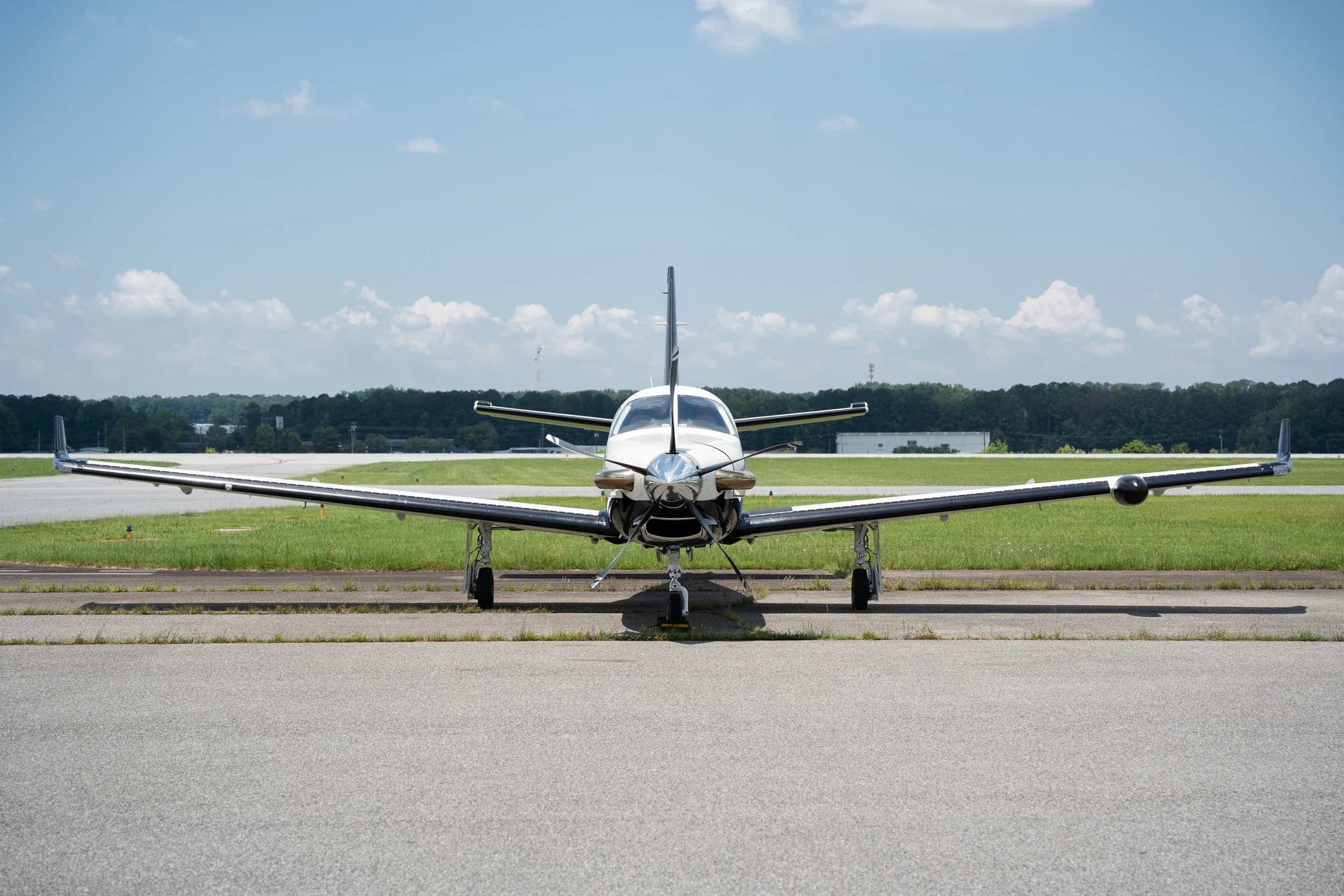 A front view of a white and black TBM 960 aircraft with its wings spread, parked on an airport tarmac with a runway in the distance.
