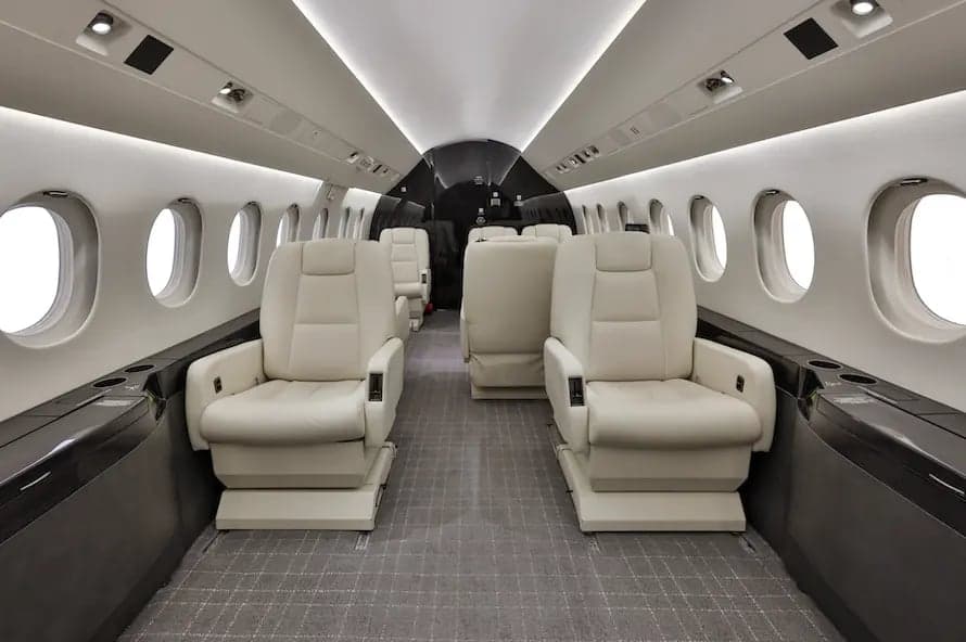 Aircraft cabin with cream-colored seats facing each other.