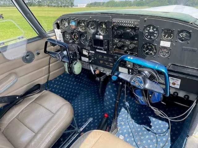 Interior view of a light aircraft cockpit with instrument panel, yokes, and brown seats.