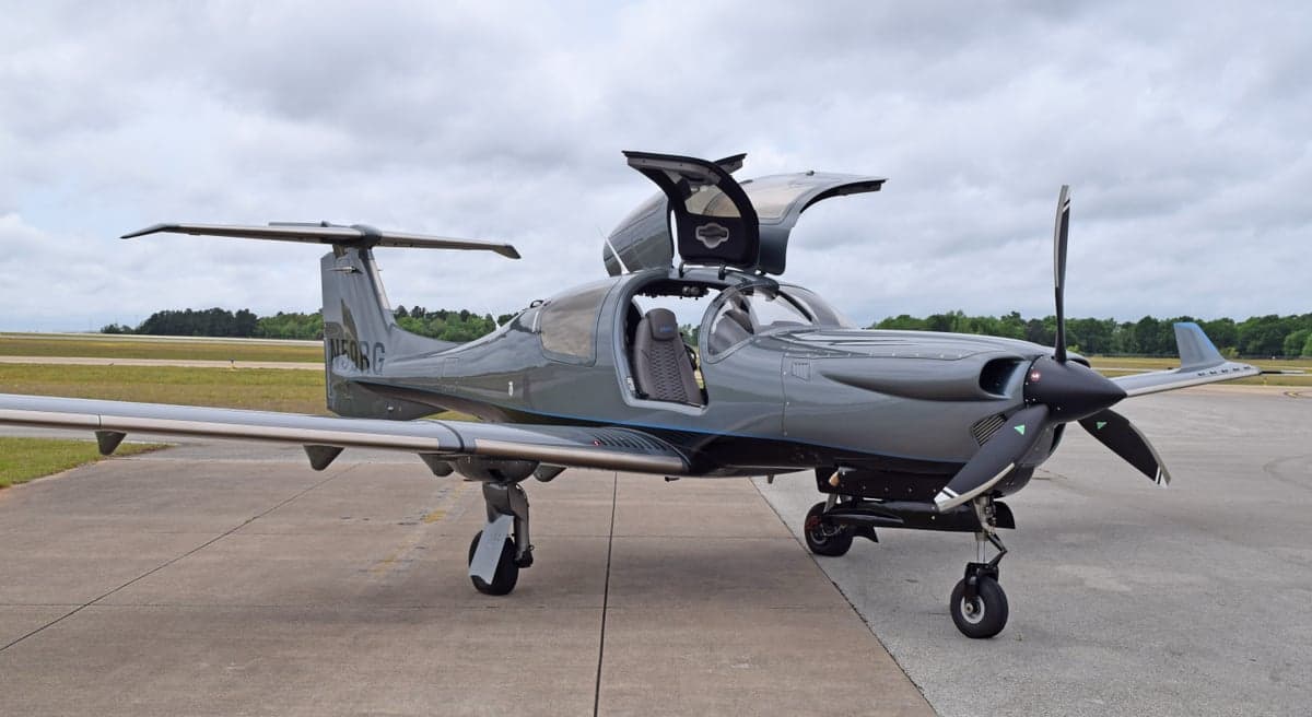 A gray Diamond DA50 RG aircraft, registration N59RG, with its gull-wing doors open, parked on an airfield.